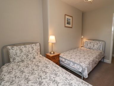 A bedroom with two single beds with floral bedding a wooden nightstand and lamps at Jasmine Cottage in Lesbury near Alnmouth
