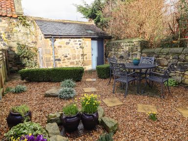 A small stone building with a blue door in a garden with stone walls metal table and chairs and flower pots at Jasmine Cottage Lesbury near Alnmouth