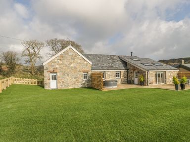 A stone house with a grassy lawn and wooden fences at Horseshoe Cottage in Abersoch