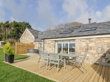 An outdoor wooden deck with metal table and chairs by a stone house with skylights at Horseshoe Cottage in Abersoch