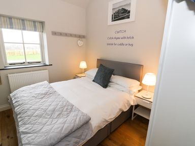 A bedroom with a double bed two bedside tables with lamps a window and a wall decal at Horseshoe Cottage in Abersoch