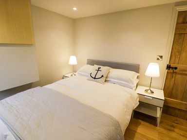 A bedroom with a double bed a pillow with an anchor symbol two bedside tables with lamps and a wooden door at Horseshoe Cottage in Abersoch