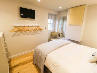 A bedroom with a bed a wall-mounted TV a wooden chair a full-length mirror and wooden hangers on hooks at Horseshoe Cottage in Abersoch