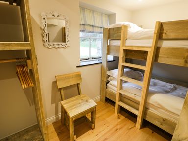A small bedroom with bunk beds a wooden chair a window with striped blinds and an open closet with hangers at Horseshoe Cottage in Abersoch