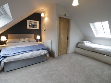 A bedroom with a double bed and a single bed under slanted ceilings at Horseshoe Cottage in Abersoch