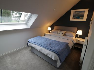 A bedroom with a double bed blue blanket bedside tables with lamps and a skylight window at Horseshoe Cottage in Abersoch