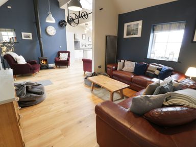 A living room with leather sofas cushions and a wooden coffee table next to a wood stove and burgundy armchairs at Horseshoe Cottage in Abersoch