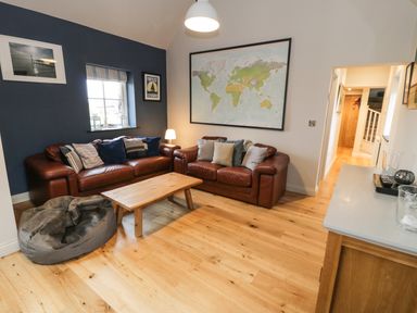 A living room with two brown leather sofas a wooden coffee table a gray bean bag a large world map on the wall and wooden flooring at Horseshoe Cottage in Abersoch