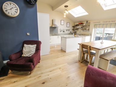 A kitchen and dining area with wooden table and chairs a burgundy armchair and skylights at Horseshoe Cottage in Abersoch