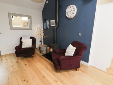 A sitting area with two armchairs a wood-burning stove and a wall clock at Horseshoe Cottage in Abersoch