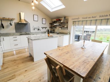A kitchen with white cabinets a wooden dining table and chairs and a skylight at Horseshoe Cottage in Abersoch