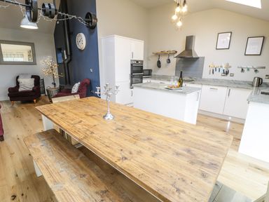 A kitchen and dining area with a wooden table and benches and white cabinets at Horseshoe Cottage in Abersoch
