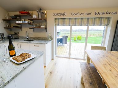 A kitchen with granite countertops open wooden shelves a dining table and sliding glass doors leading outside at Horseshoe Cottage in Abersoch