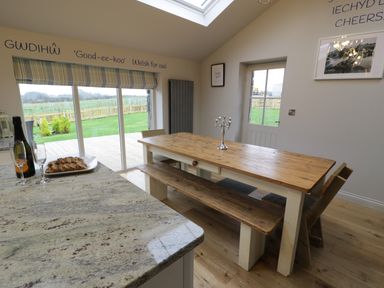 A dining area with a wooden table and bench next to large sliding glass doors showing a garden at Horseshoe Cottage in Abersoch