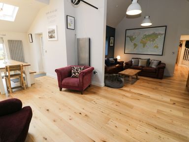 An open living area with wooden floor a red armchair a dining table with wooden chairs leather sofas a wooden coffee table and a world map on the wall at Horseshoe Cottage in Abersoch