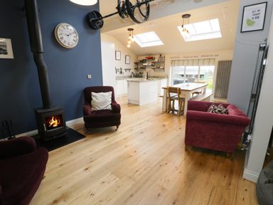 An open living and kitchen area with wood flooring a wood burning stove armchairs a dining table and skylights at Horseshoe Cottage in Abersoch