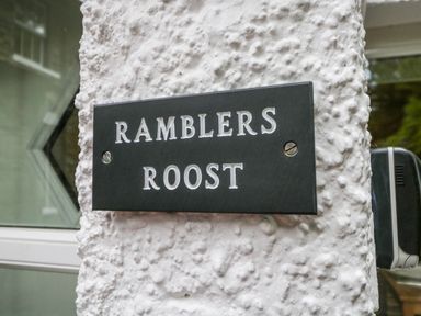 A black sign with white letters saying Ramblers Roost mounted on a textured white wall outside a building at Ramblers Roost in Grasmere