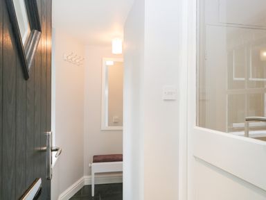 A small hallway with a dark door open a white wall a mirror a bench and a coat hook at Ramblers Roost in Grasmere
