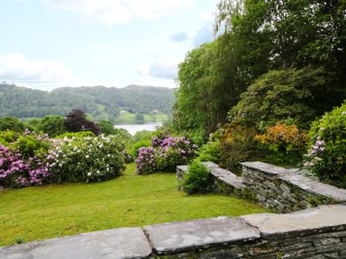 A garden with flowering bushes and stone walls overlooking a lake and hills at Ramblers Roost in Grasmere