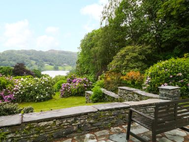 A garden with flowering bushes and trees overlooking a lake and hills at Ramblers Roost in Grasmere