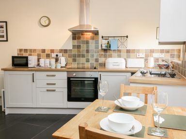 A kitchen with a wooden dining table set with bowls wine glasses and table mats at Ramblers Roost in Grasmere