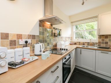 A kitchen with a wooden countertop white cabinets a stove a sink and a window at Ramblers Roost in Grasmere
