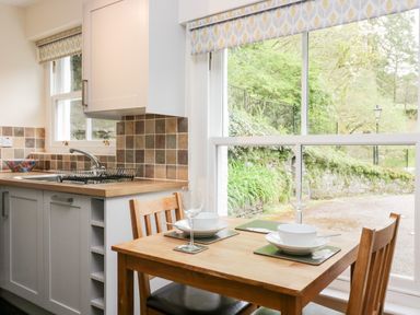 A kitchen with a wooden dining table set for two and a sink with tiled backsplash at Ramblers Roost in Grasmere