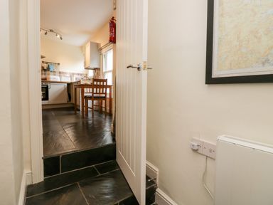 A kitchen with a wooden table and chairs tiled floor and a partially open door at Ramblers Roost in Grasmere