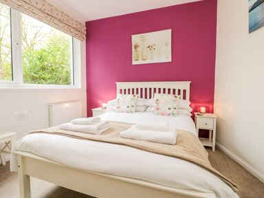 A bedroom with a double bed with floral pillows and folded towels with a purple accent wall at Ramblers Roost in Grasmere