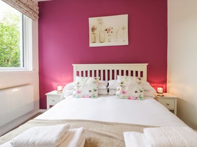 A bedroom with a double bed with floral pillows and white bedding against a purple wall at Ramblers Roost in Grasmere