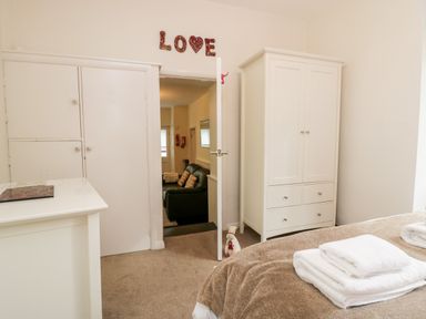 A bedroom with white wardrobes a bed with folded towels and an open door showing a living room with a sofa at Ramblers Roost in Grasmere