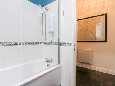 A bathroom with a bathtub and shower heater next to a hallway with a wall map and radiator at Ramblers Roost in Grasmere