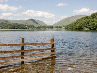 A wooden fence partially submerged in a lake with hills and trees in the background at Ramblers Roost in Grasmere