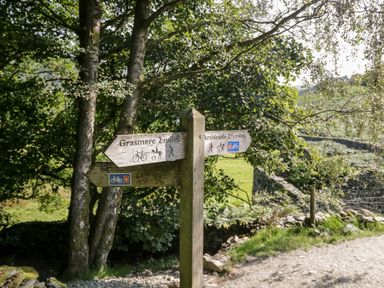 A wooden signpost on a gravel path showing directions to Grasmere and Ambleside with trees and stone walls nearby at Ramblers Roost in Grasmere