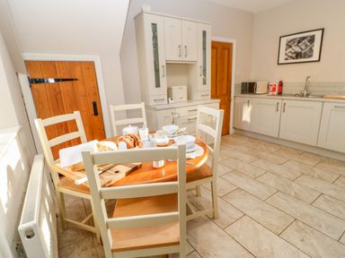 A kitchen with a wooden dining table and chairs white cabinets and wooden doors at East Farmhouse Cottage in Humshaugh near Hexham