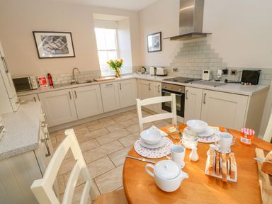 A kitchen with white cabinets a dining table set with tea crockery and toasted bread at East Farmhouse Cottage Humshaugh near Hexham