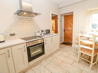 A kitchen with cabinets a built-in oven a dining table with chairs and a wooden door at East Farmhouse Cottage in Humshaugh near Hexham