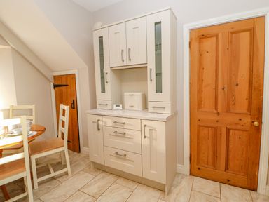 A kitchen with a wooden door a white cabinet and a dining table with chairs at East Farmhouse Cottage in Humshaugh near Hexham