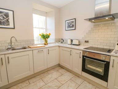 A kitchen with cabinets a sink a window flowers on a counter and an oven at East Farmhouse Cottage in Humshaugh near Hexham