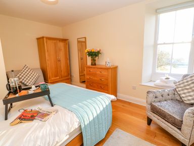 A bedroom with a bed a wooden wardrobe a chest of drawers and an armchair near a window at East Farmhouse Cottage Humshaugh near Hexham
