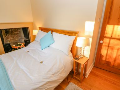 A bedroom with a wooden bed frame white bedding blue cushions bedside table with lamp and wooden door at East Farmhouse Cottage in Humshaugh near Hexham