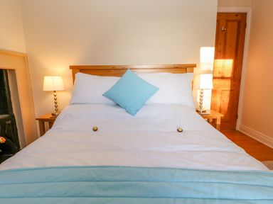 A bedroom with a wooden bed frame a white bedspread blue pillow and two bedside tables with lamps at East Farmhouse Cottage in Humshaugh near Hexham