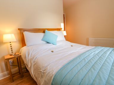 A bedroom with a wooden bed frame white bedding and blue pillows and blanket with bedside tables and lamps at East Farmhouse Cottage in Humshaugh near Hexham