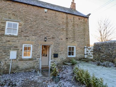 Stone exterior of a cottage with three windows a door a small garden with plants and a white wooden gate at East Farmhouse Cottage Humshaugh near Hexham