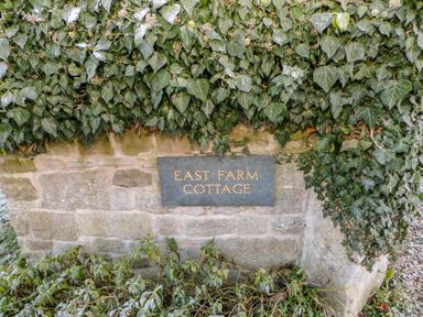 A stone wall with ivy and a sign reading East Farm Cottage at East Farmhouse Cottage in Humshaugh near Hexham