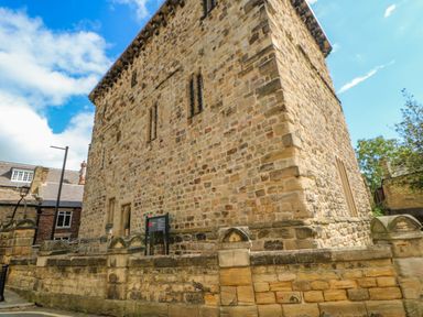 A stone building with small windows and a stone wall around it on a street with other buildings