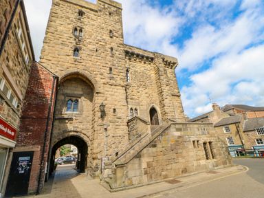 A stone historic building with an arched passageway and external stone stairs on a street