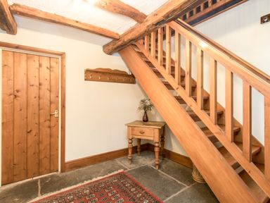 A wooden staircase next to a small wooden table with a vase and coat hooks mounted on the wall at Riven Oak in Lyth Valley near Levens