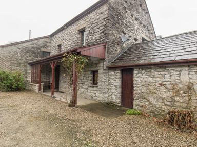 A stone exterior of a house with a wooden porch and a gravel driveway at Riven Oak in Lyth Valley near Levens