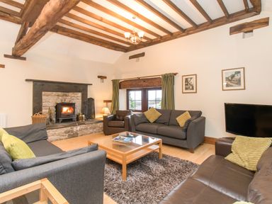A living room with a stone fireplace wooden beams sofas coffee table and a television at Riven Oak in Lyth Valley near Levens